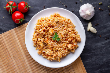 Plate of homemade delicious pilaf with chicken, fresh parsley and ripe vegetables for lunch. Top view