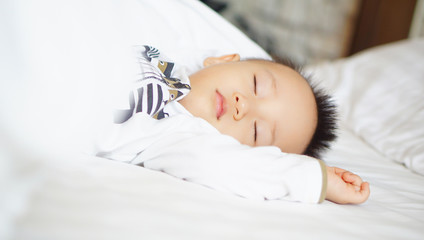 A toddler boy sleeping comfortably on white bed