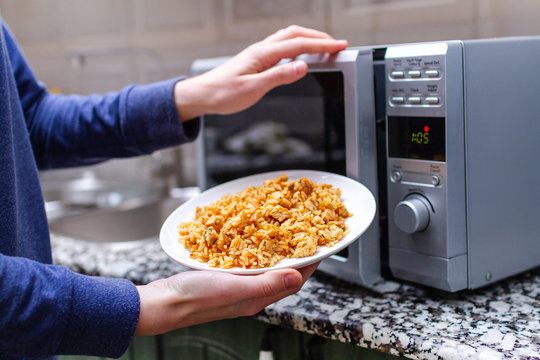 Using a microwave to warming a plate of homemade pilaf for lunch at home. Hot meal