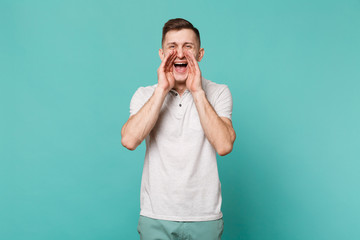 Portrait of cheerful young man in casual clothes screaming with hands near mouth isolated on blue turquoise wall background in studio. People sincere emotions, lifestyle concept. Mock up copy space.