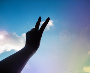 The silhouette hand showing two fingers up in the air,fighting symbol,Hand sign reach to the sky background,lens flare effect