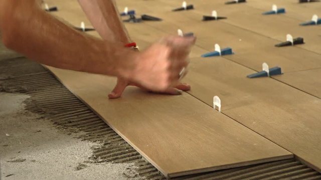 Hands of a professional tiler laying down new tile on tile mortar on the floor