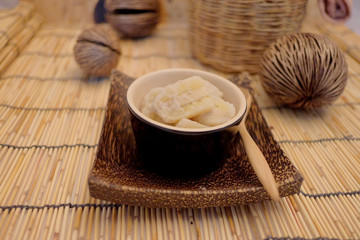 Banana in coconut milk, popular dessert from fruit, Thai style home made dessert in a cup on wood mat served after meal or appetizer, popular street food of Thailand