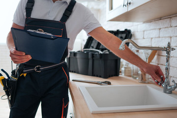 Cut view of handyman holding tool box and wrench in hands. He stand in kitchen at sink. He open...
