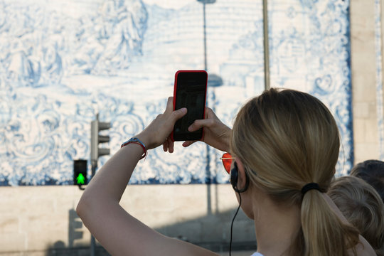 Blonde girl taking pictures on the phone at the railway station ceramic tiles. In-ear earphone is inserted from the guidance.