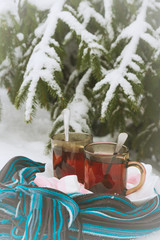 Two cups of tea with marshmallows under the tree in winter in the snow
