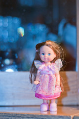 A beautiful doll girl in an airy pink dress with lace, red-.haired with blue eyes on a soft blue fabulous background.