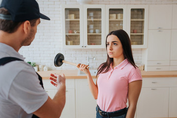 Young woman look at plumber. They stand in kitchen. She hold hangout. Guy point on sink.