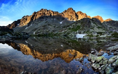 Fototapeta premium Spring or summer morning by lake in mountains. Morning beautiful nature scene. High Tatras mountain lake at reflection in water, Carpathians, Slovakia. Beautiful morning background