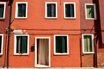 Fototapeta na wymiar Green window with shutters in Mediterranean style on red wall. Colorful houses in Burano island near Venice, Italy
