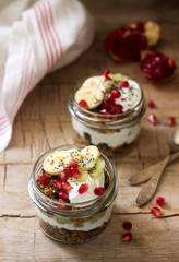 Granola with yogurt and fruit in glass jars on a wooden table. Rustic style.