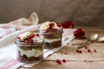 Granola with yogurt and fruit in glass jars on a wooden table. Rustic style.