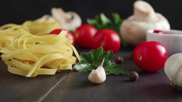 pasta ingredients on wooden table rotation depth of field.fettuccine cherry tomatoes garlic mushrooms parsley