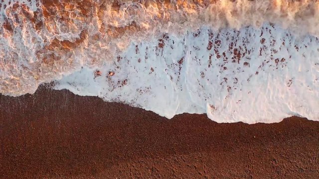 Winters Surf : Aerial image depicting two adventurers braving the freezing cold sea waters off a pebble beach. As the waves roll in, the sun low in the sky paints the foaming surf in shades of gold.