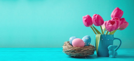 Easter holiday background with tulip flowers, eggs decoration in bird nest and bunny on wooden blue...