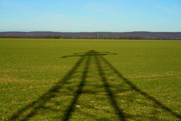 Fototapeta na wymiar Green energy concept. The shadow of an electricity pylon, high voltage transmission tower, on green agrarian land, Lower Saxony, Germany.