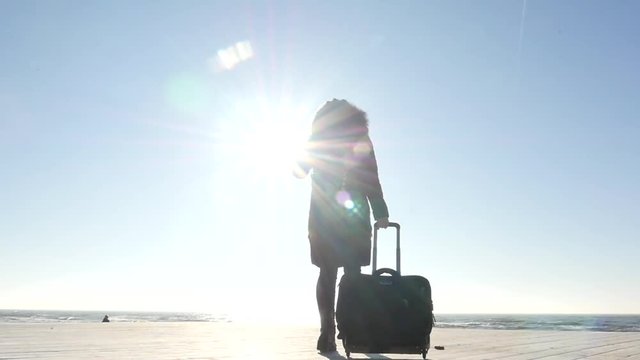 young female traveller with suitcase motion to winter seashore silhouette slow motion