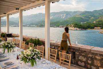 A woman looks at beautiful landscape view with sea and mountain at outdoor dining place