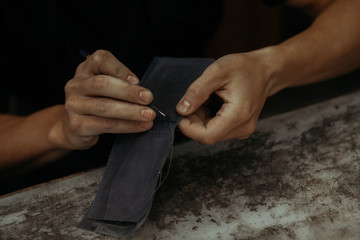 Working process of the leather wallet in the workshop. Man holding leather craft and working. Close up of leather craftsman working with natural leather. Handmade concept.