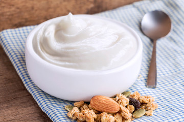 Healthy flavored yogurt in ceramic bowl with cereal and granola with cloth on wood table background.