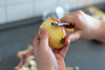 Hands peeling a cooking apple on a grey background