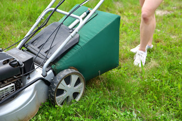Fototapeta premium Teenage girl pruning green high grass with the help of an petrol lawn mower.