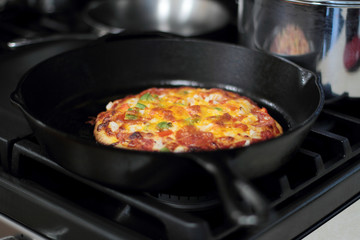 Freshly baked homemade pizza with pepperoni and chopped bell peppers in cast iron pan from the oven.
