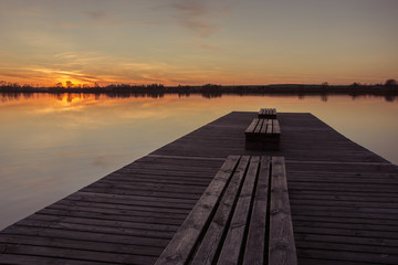 Naklejka na ściany i meble Wooden bridge with planks and sunset over a calm lake