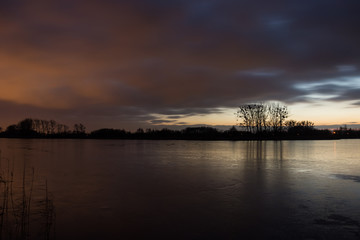 Clouds after sunset from the frozen lake and reflecting trees in the ice