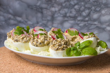 Boiled eggs stuffed with champignon mushrooms and sliced radish, parsley, salad on white plate.