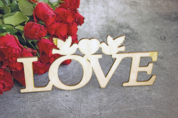 The inscription Love carved out of wood on the background of a bouquet of red roses. Love background and greeting card