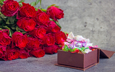 A bouquet of red roses and a box of candy next to a dark background. Congratulatory background,...