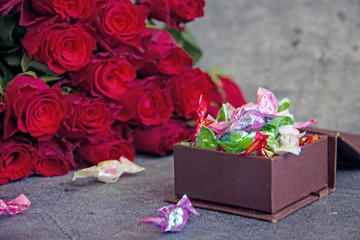 A bouquet of red roses and a box of candy next to a dark background. Congratulatory background, holiday card