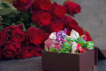 A bouquet of red roses and a box of candy next to a dark background. Congratulatory background, holiday card