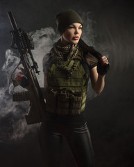 the girl in military special clothes posing with a gun in his hands on a dark background in the haze