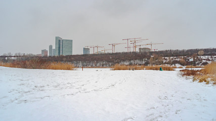 Fototapeta premium Winter in the south of Vienna Footprints leading to a park bench in Vienna's Recreational Area Wienerbergsee, and the construction site for the Biotope City and the Twin Towers in the background