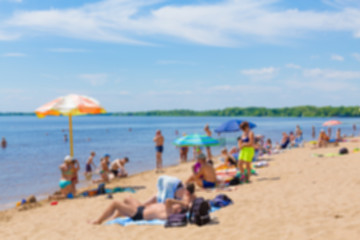 Abstract blurred image. Defocused lens, bokeh. People sunbathe and swim in the river on a sandy beach. On a Sunny summer day.