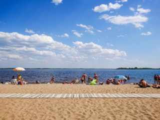 Fototapeta premium Abstract blurred image. Defocused lens, bokeh. People sunbathe and swim in the river on a sandy beach. On a Sunny summer day.