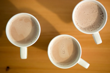 Three white cups of coffee, cocoa or latte on a wooden background on the table, closeup