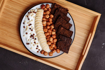 Healthy breakfast on the kitchen table. Rye bread, banana, grains, hazelnut and yogurt on black