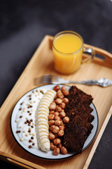 Closeup of healthy Breakfast plate with yogurt with chocolate chips, banana, rye bread, hazelnut and fresh orange juice