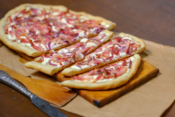 Alsatian tart flambé or Flammkuchen with bacon and onions on a dark table.