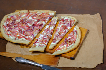 Alsatian tart flambé or Flammkuchen with bacon and onions on a dark table.