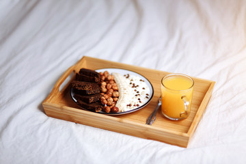 Healthy Breakfast in bed. Closeup of healthy Breakfast plate with yogurt with chocolate chips, banana, rye bread, hazelnut and fresh orange juice