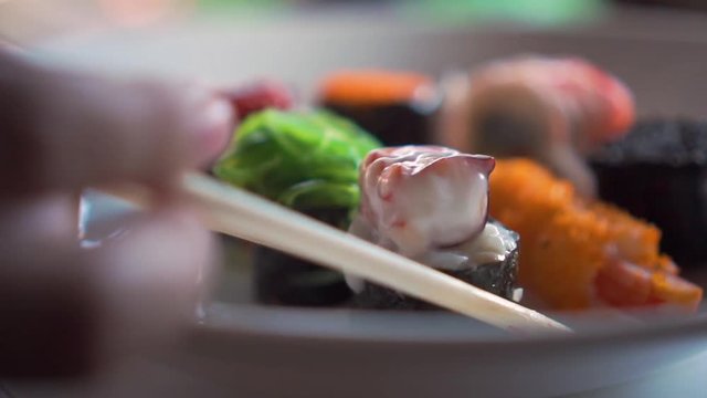 Someone use chopsticks to pick a squid with white sauce sushi. Slow Motion. Close Up.