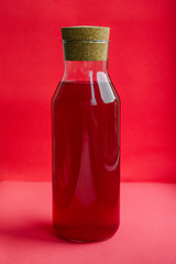 Fruit juice in glass bottle on coral background.