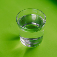 A glass of purified water on a bright green background.