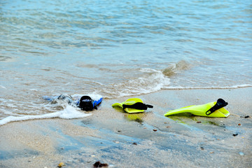 Fototapeta na wymiar Yellow and blue flippers for diving lie on the beach in the water.