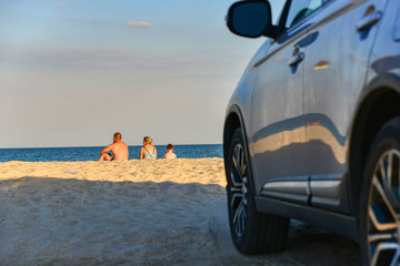 Young family with a child sitting on the beach on the background of cars.