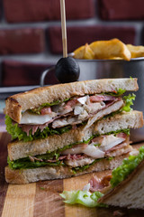 tasty chicken club sandwich with fries on wooden table